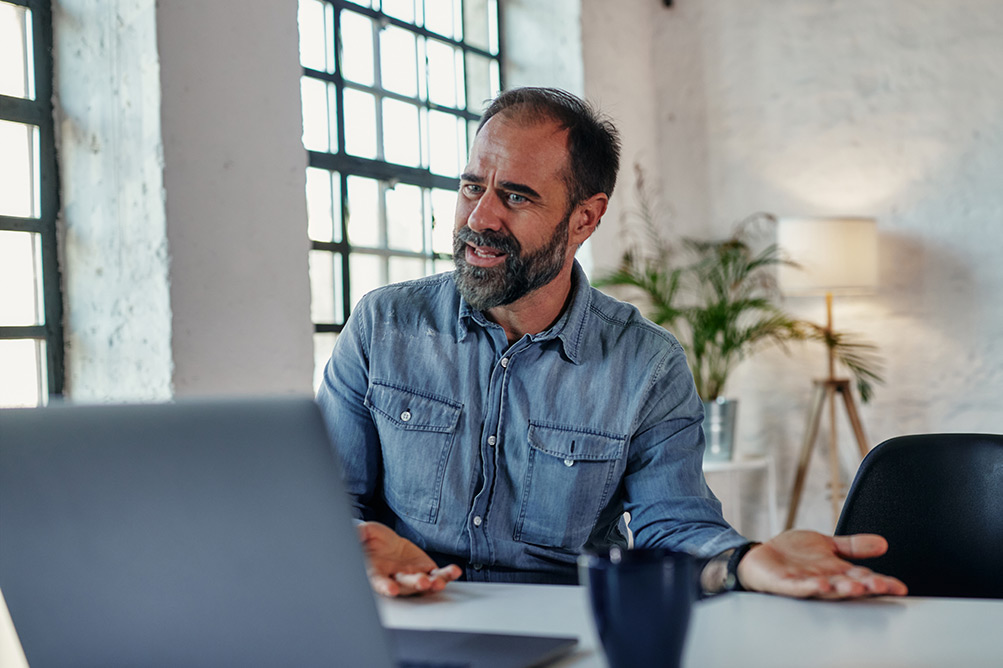 Man in online mental health appointment talking with laptop